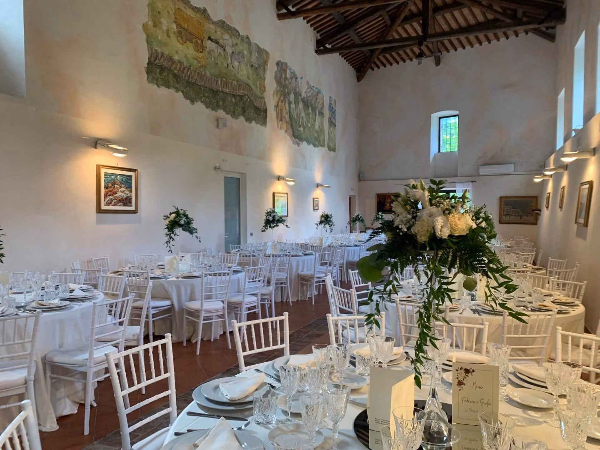 La sala per banchetti dell'Abbazia La Corte allestita con tavoli e sedie bianchi e fiori, a Micigliano in provincia di Rieti